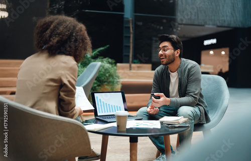 diverse team discussing charts over coffee with tablet and laptop, collaborative energy in open seating area,