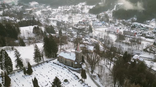 Experience the serene winter landscape surrounding the Church of St. Peter and Paul in Tanvald. Snow blankets the ground, creating a stunning view from above.
