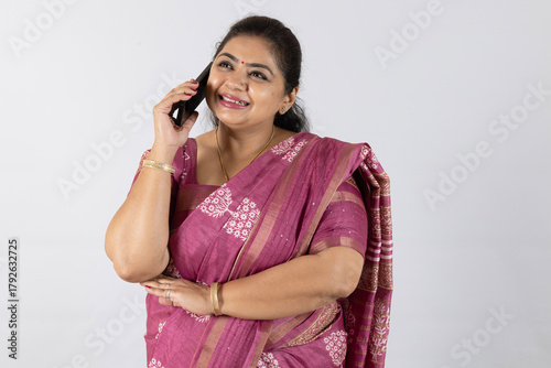 Indian attractive smiling women talking on mobile phone.. wearing traditional red color saree. phone banking and festive concepts theme isolated copyspace solid background indian concepts