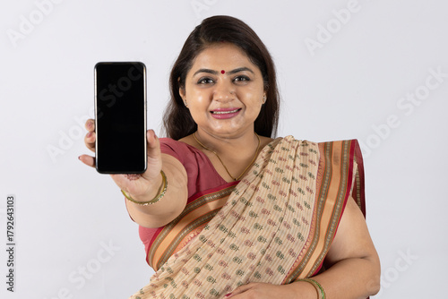 Indian happy woman showing mobile phone wearing traditional saree looking on white studio background