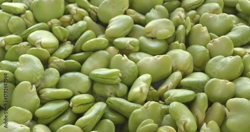 Fresh, uncooked broad beans with peeled second skin. Background texture with selective focus. Table spin, vertical video.