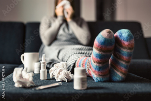 Flu or influenza. Sick and ill on cold winter. Woman with socks. Nose spray for allergy or fever medicine. Person sneezing on paper towel on home couch.
