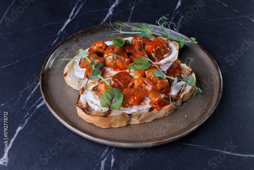 Close-up of tomato bruschetta on artisan bread slices with fresh sliced tomatoes, parmesan cheese and herbs on blue plate, cooking moment. Food preparation process, bruschetta, sandwiches.