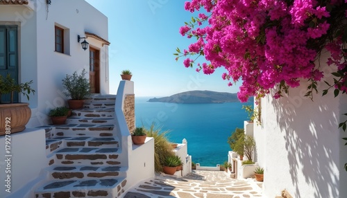 Fototapeta Naklejka Na Ścianę i Meble -  White island village street with pink bougainvillea flowers overlooks blue sea. Stone steps lead down towards ocean water under sunny sky. Charming Mediterranean town architecture.