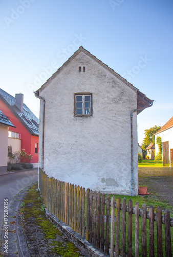 Fototapeta Naklejka Na Ścianę i Meble -  Narrow old house with a small window and wooden fence on a quiet village street.