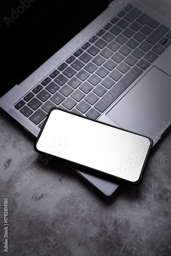 Smartphone laying on laptop keyboard with PNG screen for mockup. Mobile phone template.