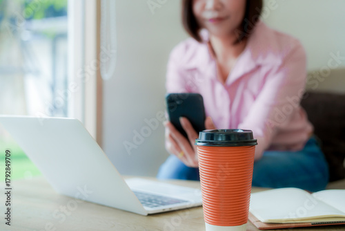 Businesswoman smiling while using laptop and talking on mobile phone at desk in office and at home or coffee shop.