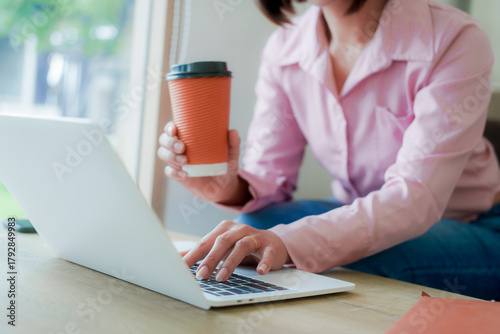 Businesswoman smiling while using laptop and talking on mobile phone at desk in office and at home or coffee shop.