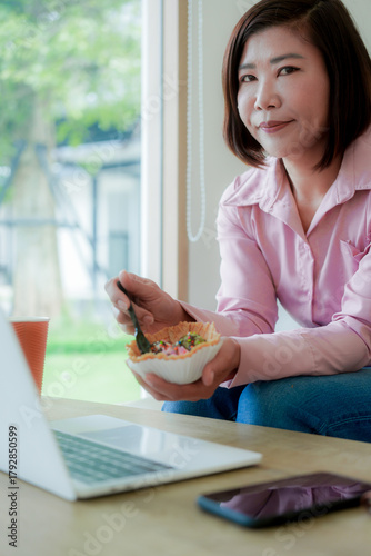 Businesswoman smiling while using laptop and talking on mobile phone at desk in office and at home or coffee shop.