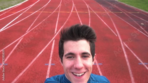 A young athlete takes a cheerful selfie slow motion video on a red running track, wearing a blue sports outfit. The scene captures energy, motivation, and the spirit of training outdoors, with bright