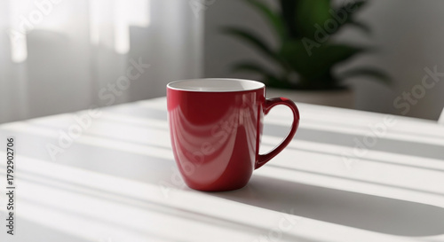 A tall deep red ceramic mug sits on a white tablecloth bathed in sunlight