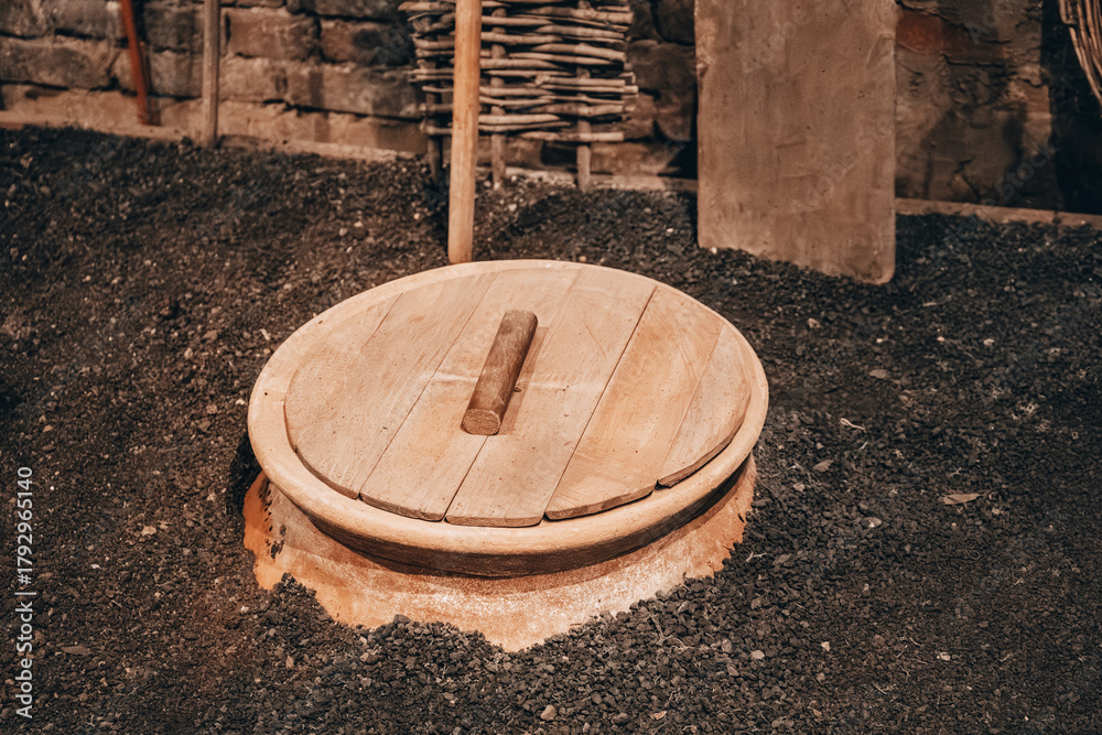 Naklejka premium Traditional Georgian clay wine vessel qvevri buried in the ground and covered with a wooden lid, symbol of ancient winemaking culture