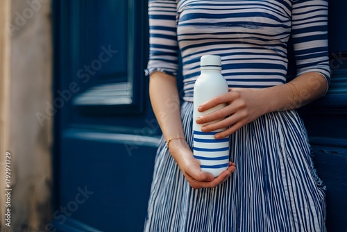 Woman in Striped Dress Holding Water Bottle Near Blue Door