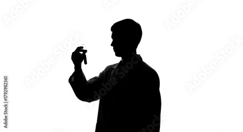 Silhouette of a scientist examining a test tube against a bright white background in a laboratory