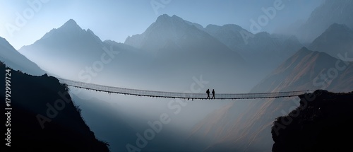 Distant figures on a suspension bridge amidst misty mountains at dawn