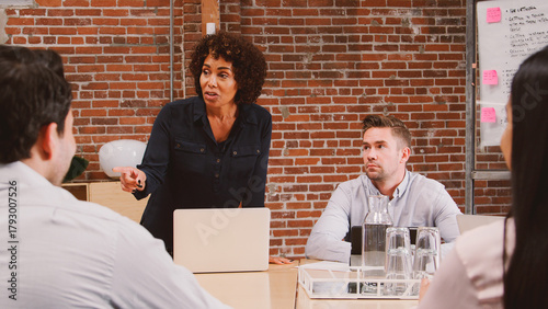 Mature Businesswoman Standing And Leading Office Meeting Around Table