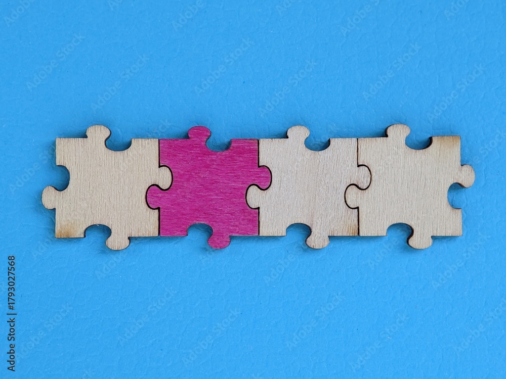 Obraz premium A row of wooden puzzle pieces lies against a bright blue background, with the center piece in pink. The image conveys teamwork, collaboration and problem-solving in a modern, colorful composition