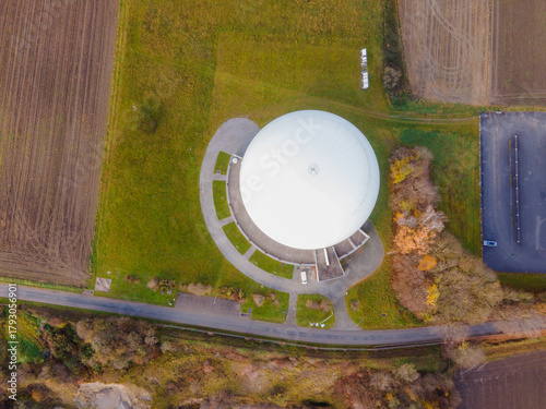 Aerial view of a pristine white radome structure nestled amid autumnal fields, where golden hues meet verdant grass, Raisting, Bayern, Germany.