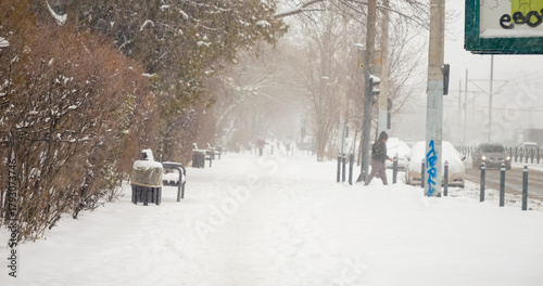 Fototapeta Naklejka Na Ścianę i Meble -  Snow falls heavily, covering the city and streets in a thick layer, making it difficult for pedestrians to navigate through the winter weather.