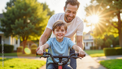 Father teaches young son to ride a bicycle in sunny neighborhood during summer  