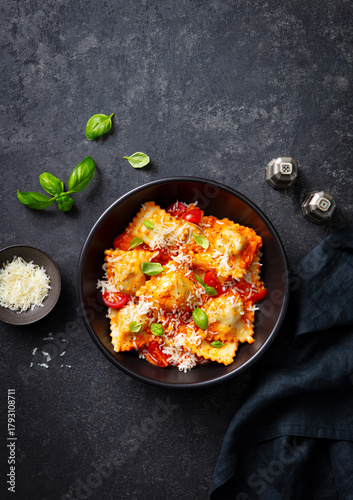 Ravioli with cheese, tomato sauce and fresh basil in black bowl. Dark grey background. Top view.