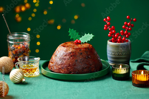 Christmas pudding, fruit cake. Traditional festive dessert. Green background with lights garland. Close up. Copy space.