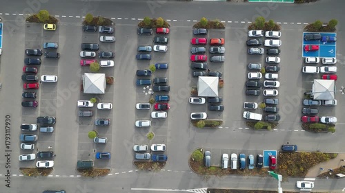 Aerial view of busy parking lot near shopping center, showcasing various vehicles in organized rows, with gradual camera zoom out revealing scene dynamics and spatial arrangement