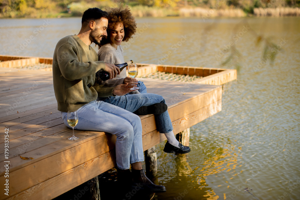 Naklejka premium Couple enjoying a peaceful moment by the lake as they sip wine under the sun