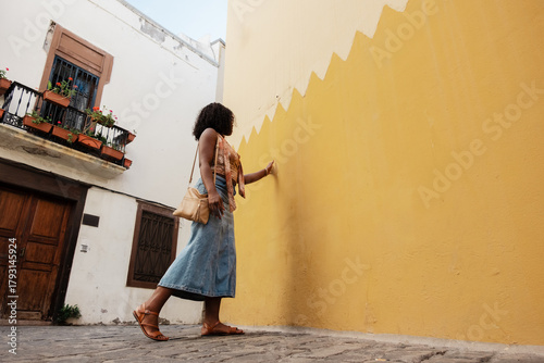 Woman touching yellow wall walking in town alley