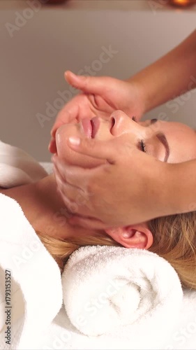 spa facial massage with caucasian woman lying on rolled towel while licensed esthetician gently massages face with oil and cream; warm candlelight, calm atmosphere, closed eyes, massage in spa center