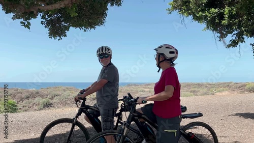Active senior couple enjoys a scenic coastal bike ride, wearing helmets give high five. Fitness, adventure, joy of outdoor activities in retirement