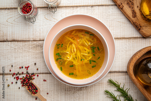 Hot chicken noodle soup with fresh herbs served in a pink bowl on a wooden table