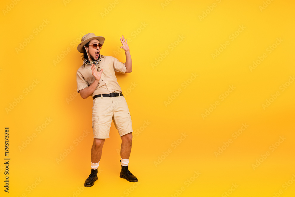 Fototapeta premium Adventurous young man in safari outfit poses against bright yellow background