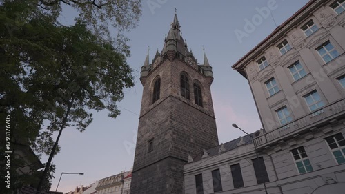 Daytime footage of Henry’s Tower, also known as Jindřišská Tower, captured from street level with surrounding historic buildings and tree branches framing the scene. Shot in Prague, Czech Republic.