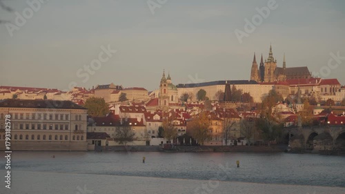 Wide sunrise footage of the historic Charles Bridge crossing the Vltava River, with a clear view of Prague Castle and St. Vitus Cathedral illuminated in the background. Shot in Prague, Czech Republic.