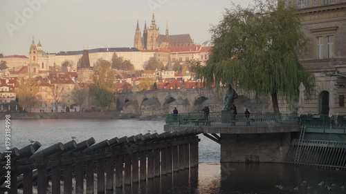 Wide sunrise footage of the historic Charles Bridge crossing the Vltava River, with a clear view of Prague Castle and St. Vitus Cathedral illuminated in the background. Shot in Prague, Czech Republic.
