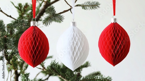 Three decorative honeycomb ornaments in red and white hanging from a Christmas tree branch.