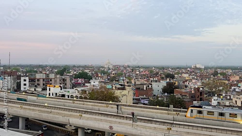 Locked shot of Metro train on elevated track passing by with the white marble Taj Mahal in the distance showing the modernization of the city of Agra with it's historical heritage