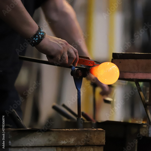A glass crafter is burning and blowing an art piece.