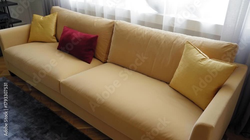 Modern yellow sofa with red and yellow pillows in cozy living room interior