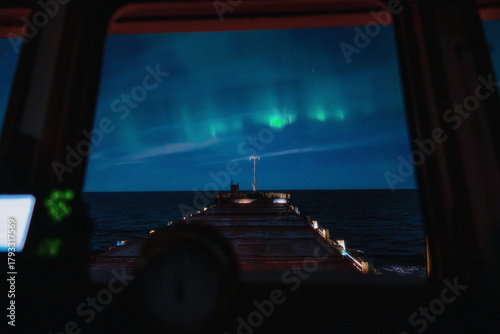 Northern lights over the open sea, viewed from the bridge of a cargo vessel at night. Aurora borealis illuminating the sky with green light, maritime navigation and ocean night scenery.