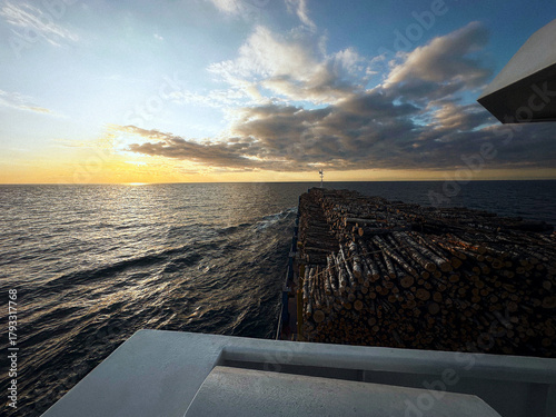 A cargo vessel transporting timber logs across the open sea at sunset. 