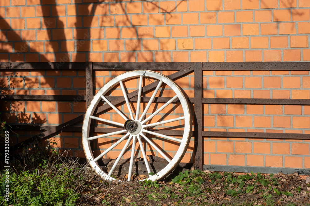 Obraz premium White wagon wheel leaning on rustic brick wall