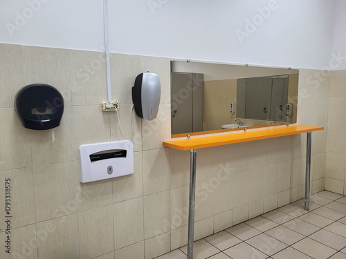 Public bathroom with a mirror, a table, a toilet paper box, and an electric hand dryer