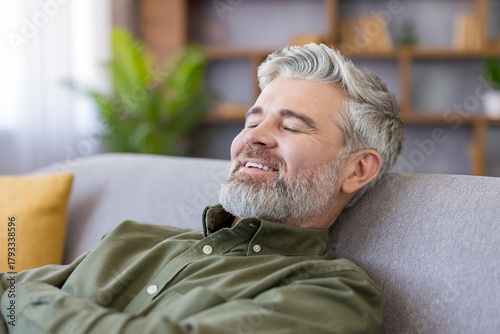 фотографія Mature man with grey hair and beard reclining on a cozy sofa at home, eyes close