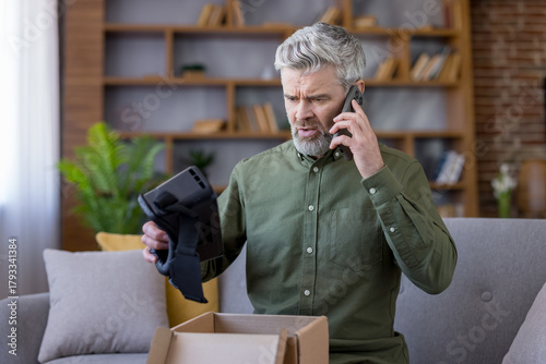 Vászonkép Mature man holding a new virtual reality headset with a perplexed expression, ma