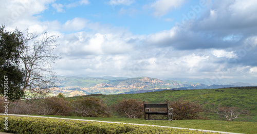 View of the rolling hills of Simi Valley, California, USA with blue skies and white clouds passing overhead and a wooden bench in the foreground