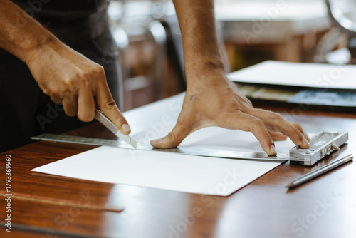 Person cutting paper using a ruler and craft knife for art project, precision hobby, or design work