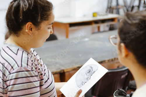 Young woman showing art drawing to friend, learning artistic skills in creative workshop, sharing ideas