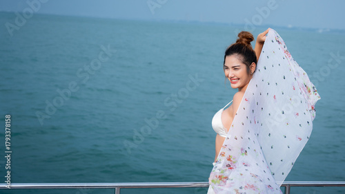 Foto Beautiful woman relaxing on yacht with blue sea background, wearing white bikini and floral shawl under sunlight